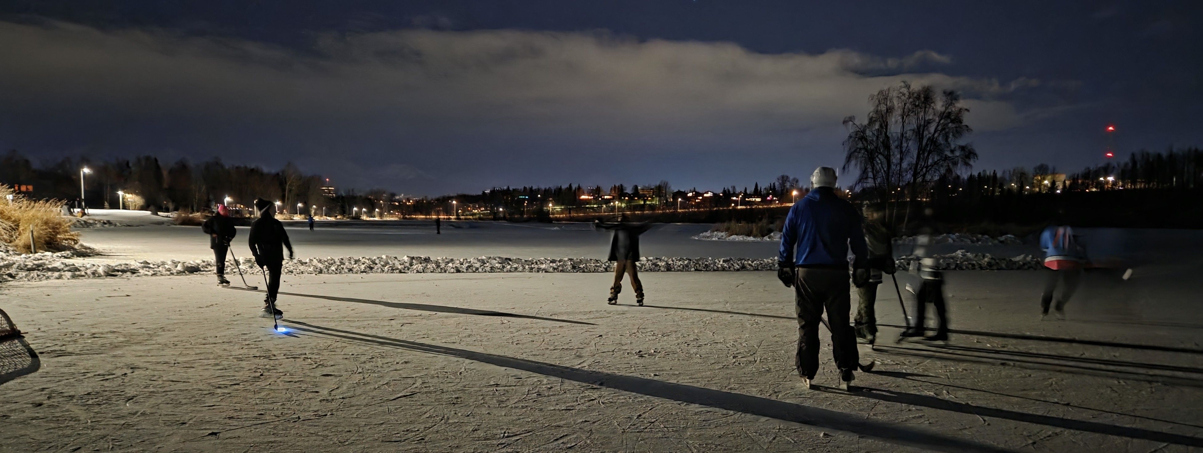 Kids playing hockey at night on a pond